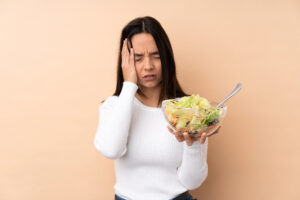 Immagine raffigurante ragazza bruna che tiene in mano un piatto di insalata e ha mal di testa