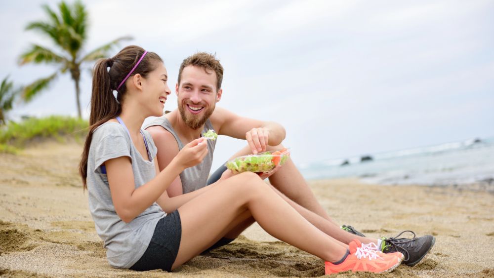 Un ragazzo e una ragazza seduti in spiaggia - Sotto questo sole cosa mangiare in spiaggia